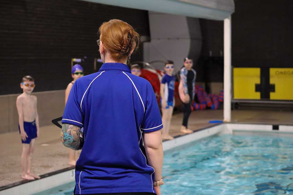 swimming teacher talking to children at the edge of a swimming pool